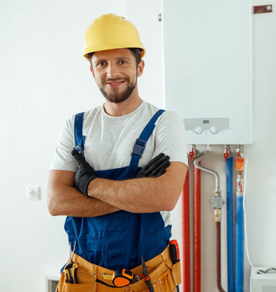 Smiling technician servicing the house heating system looking at camera while standing with arms